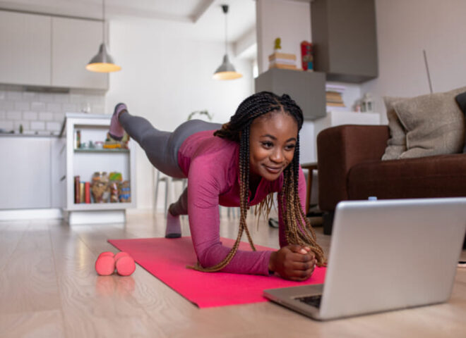 Young african america woman at home doing exercise while looking at her laptop